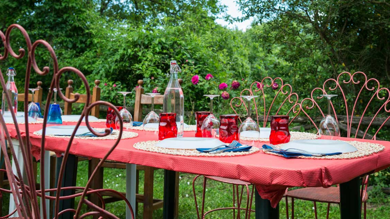A table sitting outside with plates, silverware and cups.