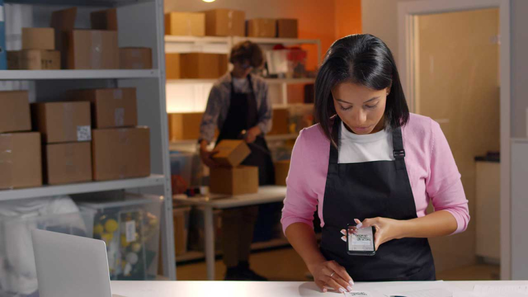A woman scanning a receipt with a cell phone in an packaging area.