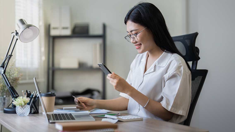 A woman holding a credit card and phone, sitting at a desk.