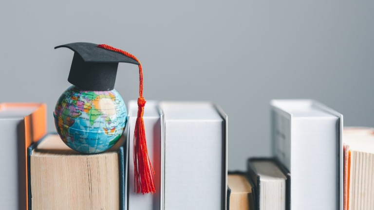 Tiny globe wearing a graduation cap, sitting atop a line of books