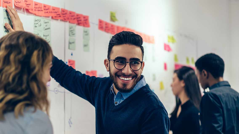 Positive young man laughing while collaborating with colleagues on creating presentation using colorful stickers for productive work in office