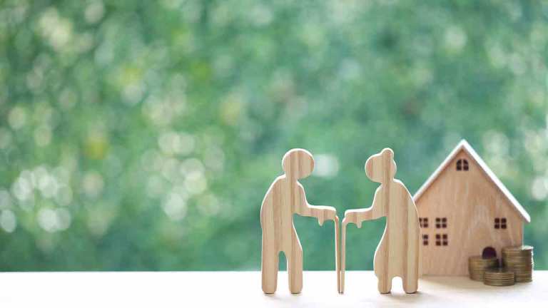 Couple wooden figures standing with a miniature house and coins, representing retirement home planning, property investment