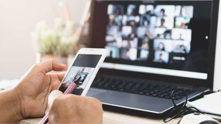hand holding phone in front of team meeting on laptop
