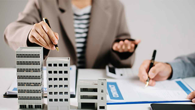 woman with a pen pointed at building models on a desk