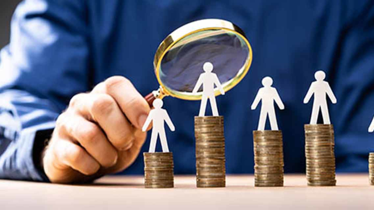 man holding magnifying glass over paper cutouts of a person standing on top of coins