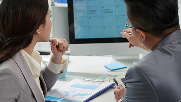 Two business professionals looking at a calendar on a computer.
