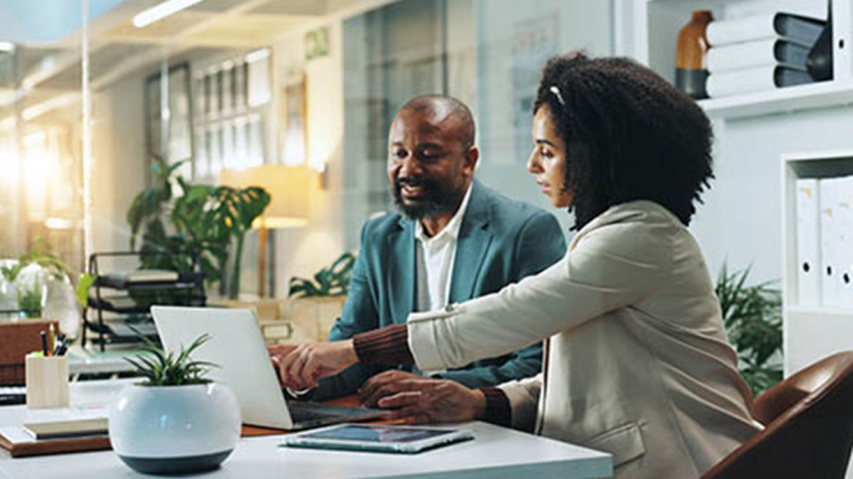 Two business professionals sitting at a desk looking at a laptop.
