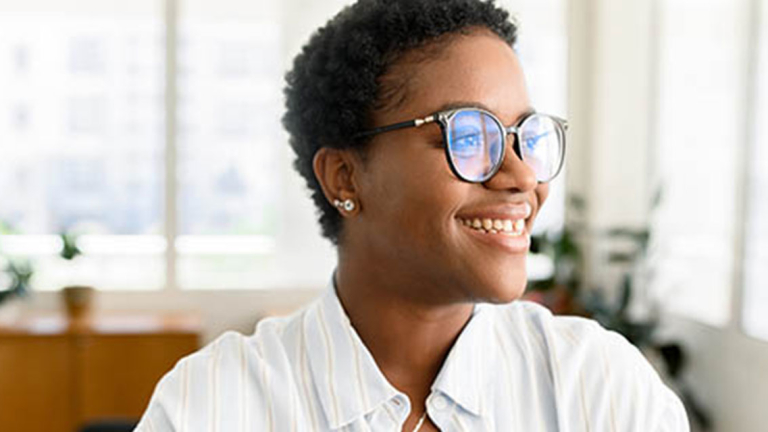 A woman in glasses in an office, smiling.