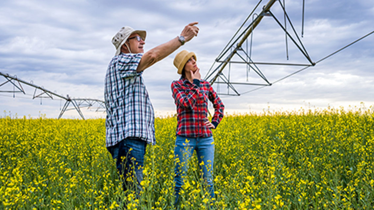 A man and woman in a field of flowers looking up at a large irrigation system.