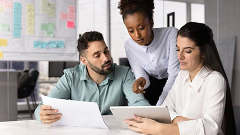 Business professionals gathered around a table looking at a tablet and papers.