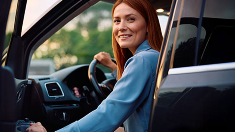 A woman sitting in the driver seat of a car with the door cracked open.