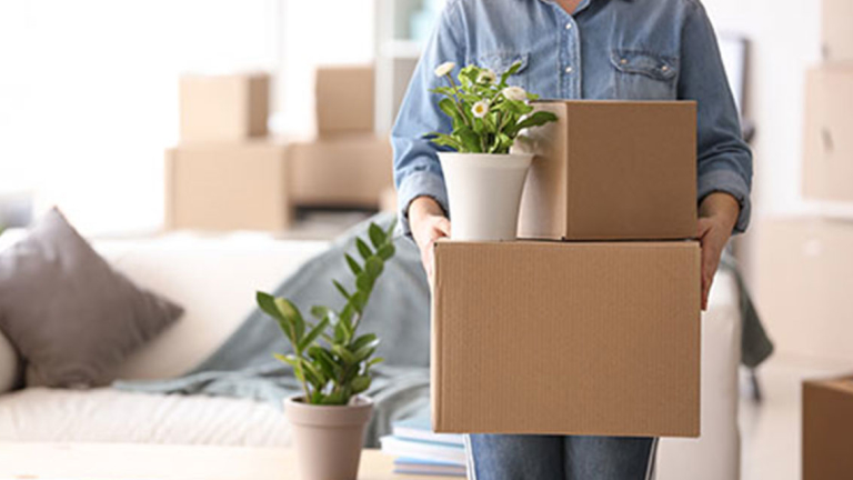 A woman holding a couple boxes and a plant.
