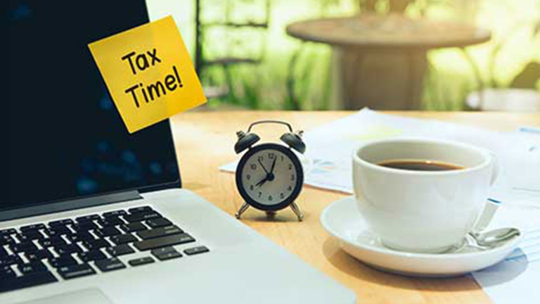 A cup of coffee, mini alarm clock, and a laptop with a sticky note on it.