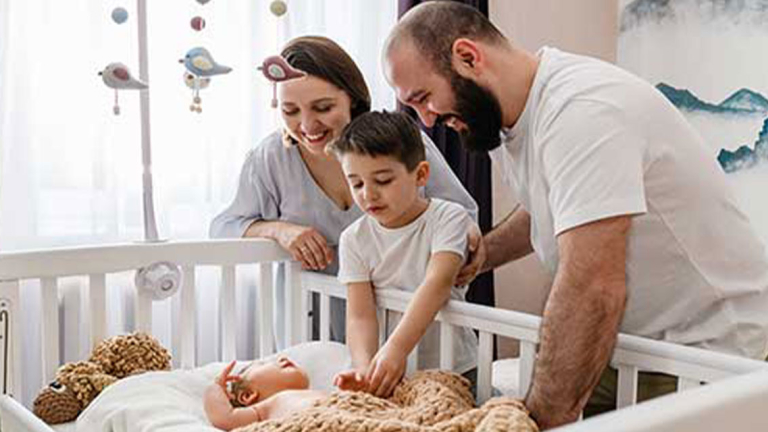 A man, woman, and young boy looking at a baby in a crib and smiling.