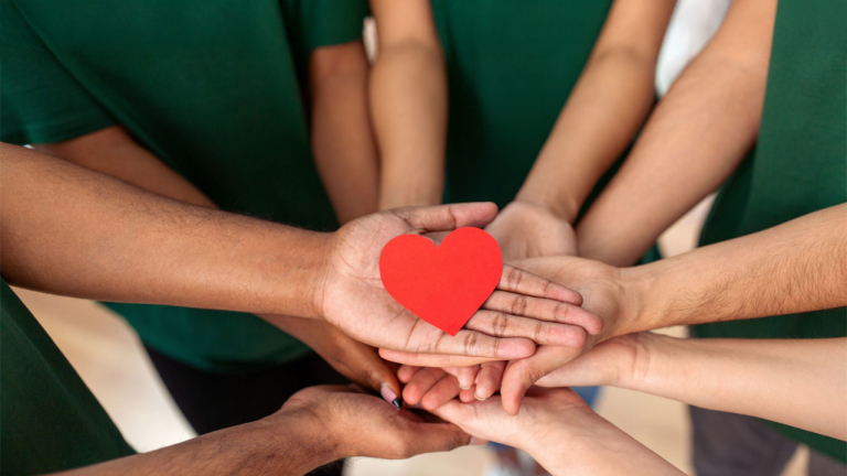 Peoples stacked on top of each other in a circle with a paper heart in the middle.