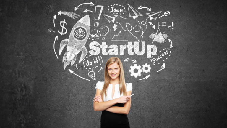 A business professional, holding chalk, standing with arms crossed in front of a chalk board.