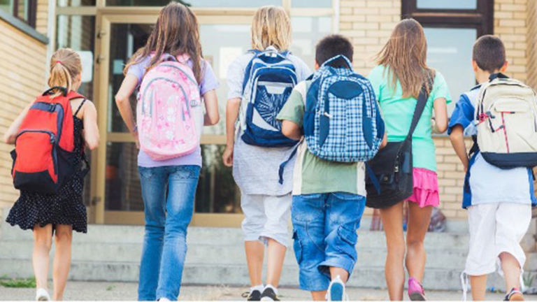 Kids wearing backpacks walking into school.