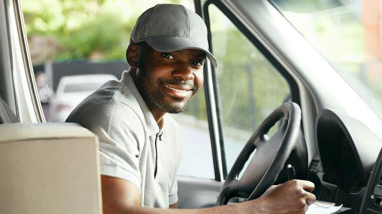 A delivery driver with a box next to him sitting in a truck.