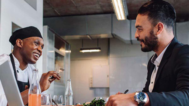 A restaurant worker and man sitting at a table, laughing