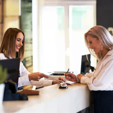 Two women at a concierge desk with paper and pen and a bell.