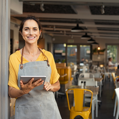 Female business owner in yellow shirt standing near a restaurant door.