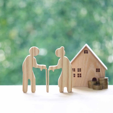 Couple wooden figures standing with a miniature house and coins, representing retirement home planning, property investment