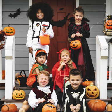 set of various age children sitting and standing on steps in halloween costumes and surrounded by halloween decorations