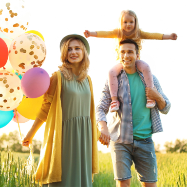 family of three standing outside smiling and holding balloons
