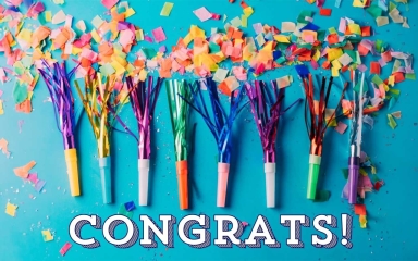 Party streamers and confetti laid on a table overtop of the word "Congrats!".
