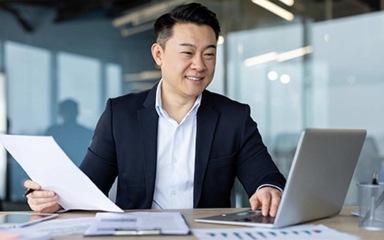man with paper in hand and typing on laptop