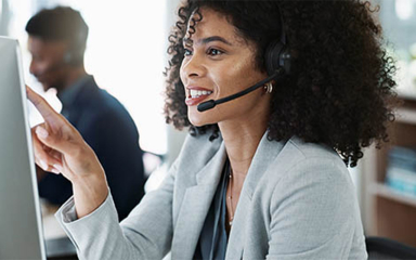 A woman in a headset pointing at a computer monitor.