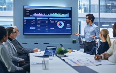 Professionals in a meeting room looking at a giant screen with graphs and numbers.