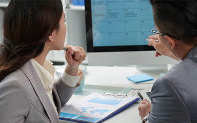 Two business professionals looking at a calendar on a computer.