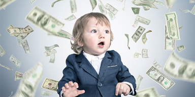 A baby wearing a suit with money falling all around them.
