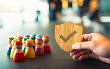 A hand holding a wooden shield with a checkmark next to wooden people.