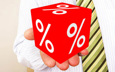A man in a dress shirt and tie holding a big red die with percentage icons on it.