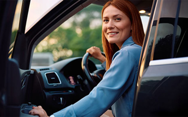 A woman sitting in the driver seat of a car with the door cracked open.