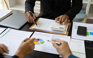 People at a table with papers, graphs, mobile phones, laptops and pens.