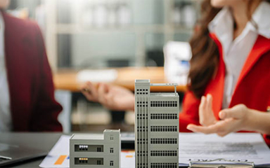 Two business professionals talking with a model of a building on a table between them.