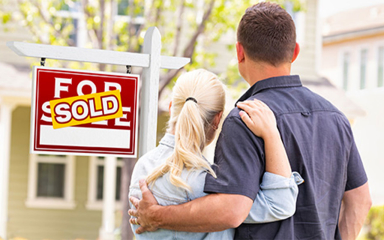 Man and woman hugging in front of a For Sale Sold sign.