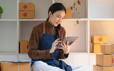 A female wearing an apron and sitting down using a tablet.