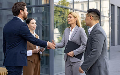 Business professionals in front of an office building, shaking hands.