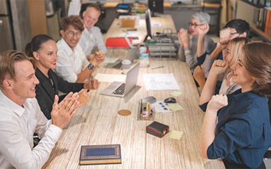 Business professionals laughing and clapping while sitting at a long table.