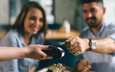 A man holding out a credit card over a scanner behind held by a woman's hand.