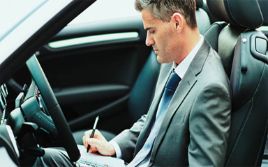 A business professional sitting in a car writing on a notepad.