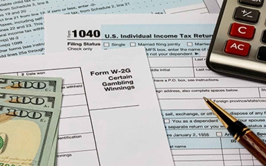 Tax forms laid out with money and office supplies scattered around it.