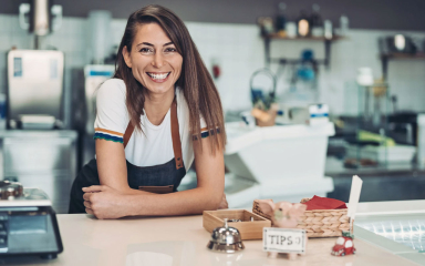 A woman in an apron leaning on a counter in a kitchen.