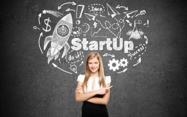 A business professional, holding chalk, standing with arms crossed in front of a chalk board.