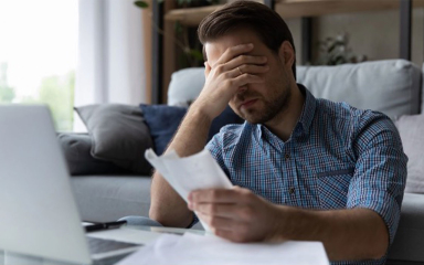 A man holding receipts in one hand with his other hand over his face.