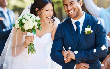 A newly married couple holding hands and laughing at a wedding.